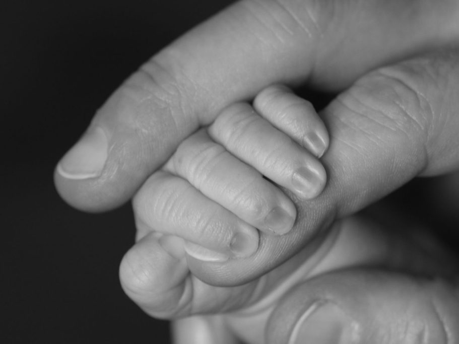 Die Hand eines Neugeborenen umschließt fest den Finger eines Erwachsenen.