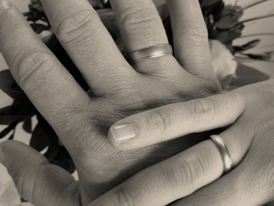 Zwei übereinander liegende rechte Hände, die jeweils am Ringfinger einen schlichten Ring tragen